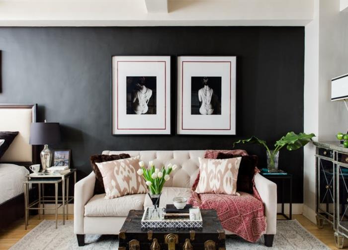paveikslai su nuotraukomis, smėlio spalvos sofa, vintažinis lagamino stalas, pilkas kilimas, juoda siena svetainėje
