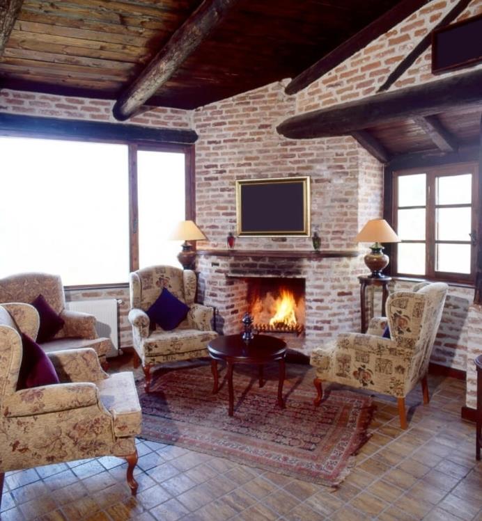 plytų siena, akmens grindys, senoviniai foteliai, mažas rytietiškas kilimas, medinis kavos staliukas, medinis karkasinis namas, kaimiška svetainė