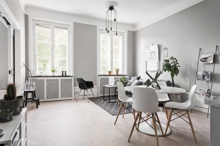 gri ve beyaz oturma odası dekoru, inci grisi duvar, beyaz masa ve İskandinav sandalyeli yemek alanı, gri kanepe ve geometrik İskandinav halısı, gri ve beyaz İskandinav mobilyaları