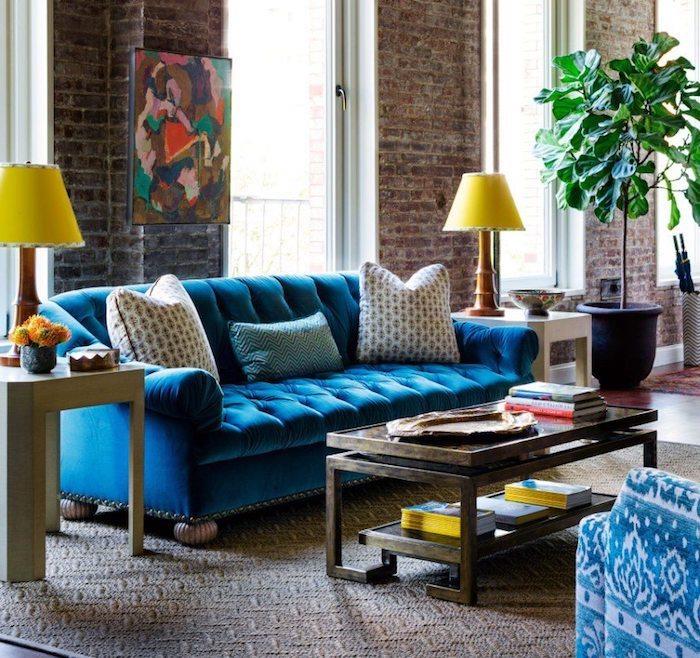 opečna stena in velika okna v industrijskem slogu dnevna soba z modrim kavčem in izvirno leseno mizo na sivo -beli preprogi, zelena rastlina v velikem loncu
