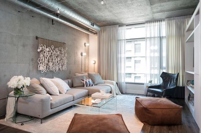 dnevna soba v industrijskem slogu s sivim kavčem, zanimivo dekoracijo sten, betonsko steno, umazano belo preprogo in rjavimi stolčki