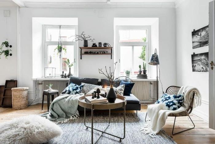 Skandinaviško stiliaus svetainė su baltomis sienomis žalvarinis boso stalas pilka sofa kokonuojanti kėdė pilkas kilimas