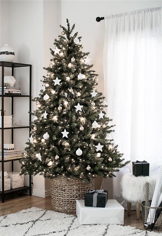 bir rattan sepete yerleştirilmiş beyaz Noel süsleri ile İskandinav minimalist tarzında dekore edilmiş doğal bir Noel ağacı, beyaz ve siyah İskandinav oturma odası