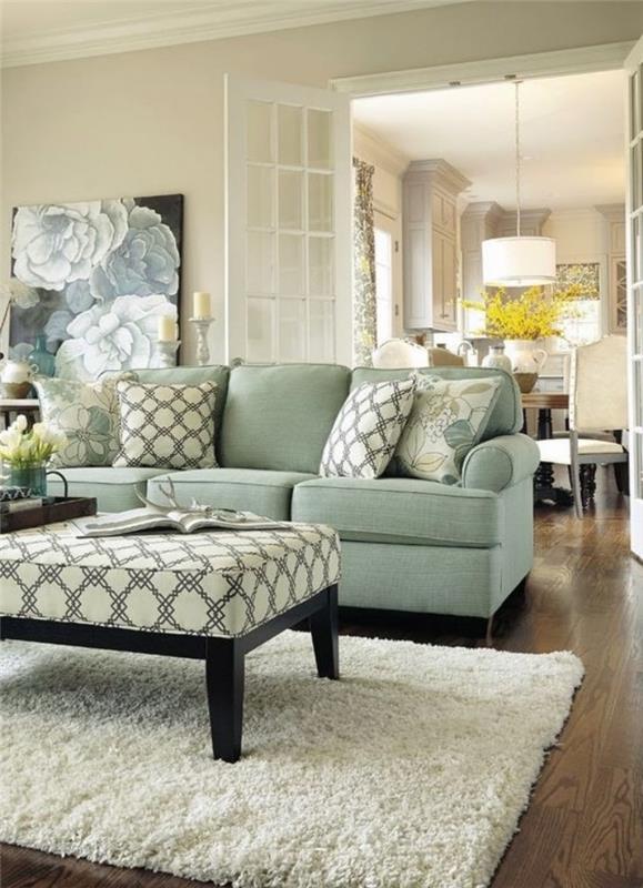 vandens žalia svetainės modelis, su žalia sofa, baltas kilimas, rudas stalas su balta pagalve su geometriniais raštais, rudas parketas, dekoratyvinė plokštė su gėlių raštais