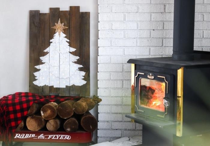 Geri kazanılmış bir ahşap paletten DIY ahşap Noel ağacı, rustik bir dekorda şöminenin yanına yerleştirilmiş geri kazanılmış bir ahşap masa üzerinde beyaz boyalı Noel ağacı