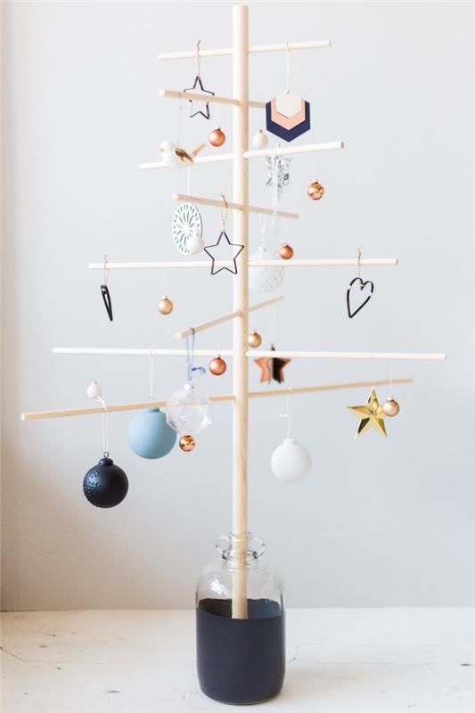 ahşap bir Noel ağacının orijinal ve minimalist modeli, yarı şeffaf bir cam vazoya yerleştirilmiş ve çok sayıda Noel askısıyla süslenmiş doğal bir ahşap destek