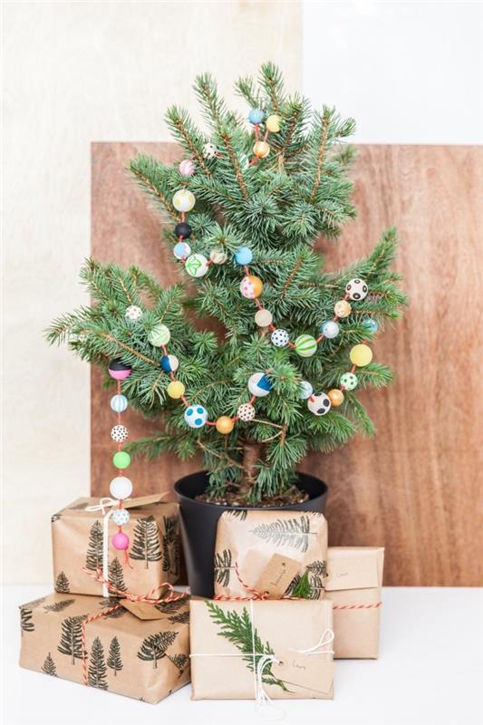 Doğal ve İskandinav ruhu kutlaması için boyalı renkli desenlere sahip ahşap boncuklardan yapılmış bir DIY çelenk ile bir tencerede doğal Noel ağacı dekorasyonu
