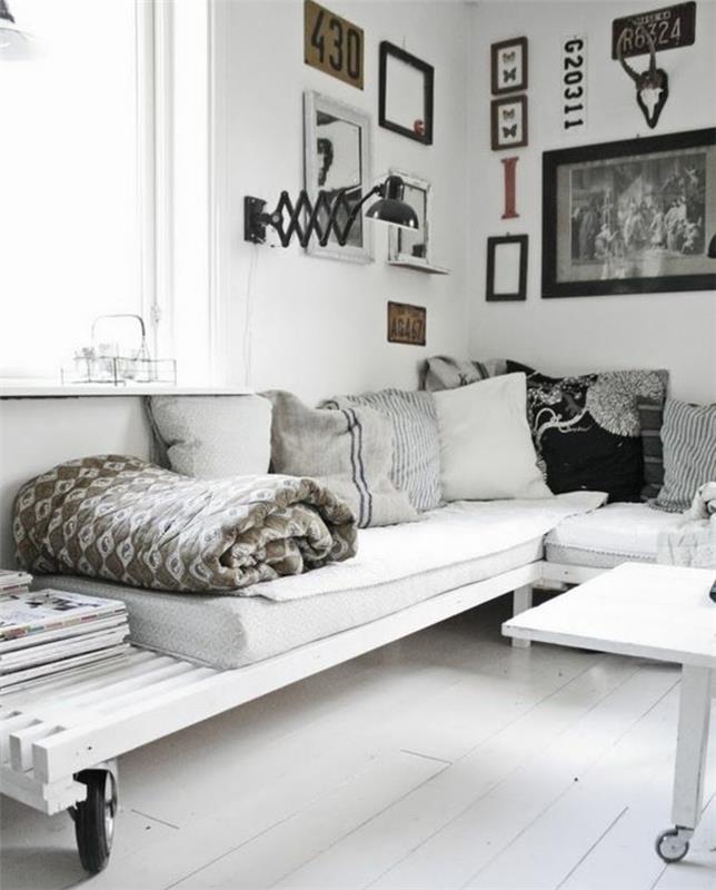 Šiaurės stiliaus kambarys su baltomis medinėmis grindimis, baltomis sienomis su daugybe įrėmintų vaizdų ir baltais baldais iš padėklų