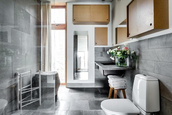 retro kopalnica s starinskim skandinavskim lesenim pohištvom in dekorjem ter sivimi ploščicami na tleh in stenah ter voskanim betonskim umivalnikom