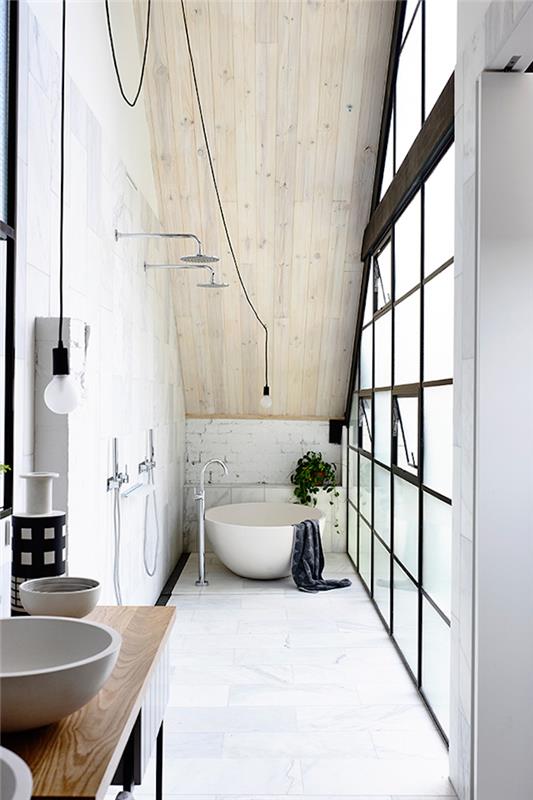 kopalnica ozke dolžine, opremljena pod podstrešjem v skandinavskem podstrešju z industrijsko kovinsko okno, okroglo kadjo, leseno streho in okroglimi umivalniki na tleh iz belega marmorja