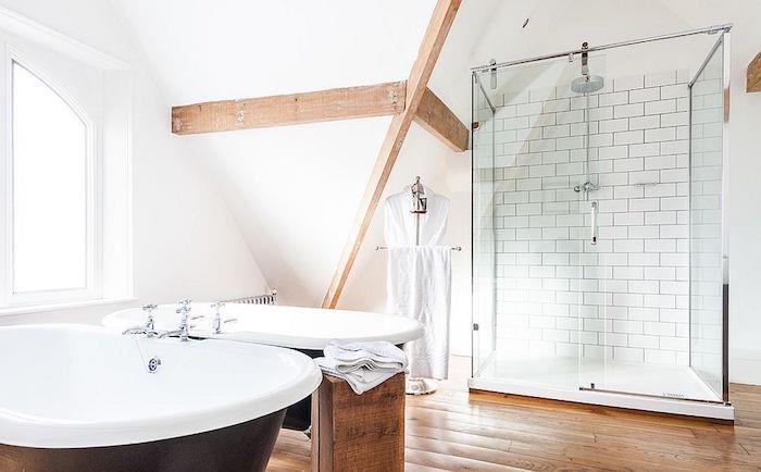 Skandinavska kopalnica s švedskim dekorjem s parketom in izpostavljenimi lesenimi tramovi z oblikovalsko dvojno rjavo samostoječo kadjo in stekleno prho z belimi stenami