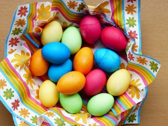spalvotų kiaušinių Velykoms pavyzdys su valgomais dažais ir šaukštu acto, išdėstyti ant lėkštės, padengtos įvairiaspalve servetėle