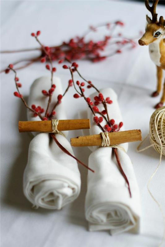 originaliai surištos baltos servetėlės, šakos su raudonomis uogomis, dekoratyviniai elniai