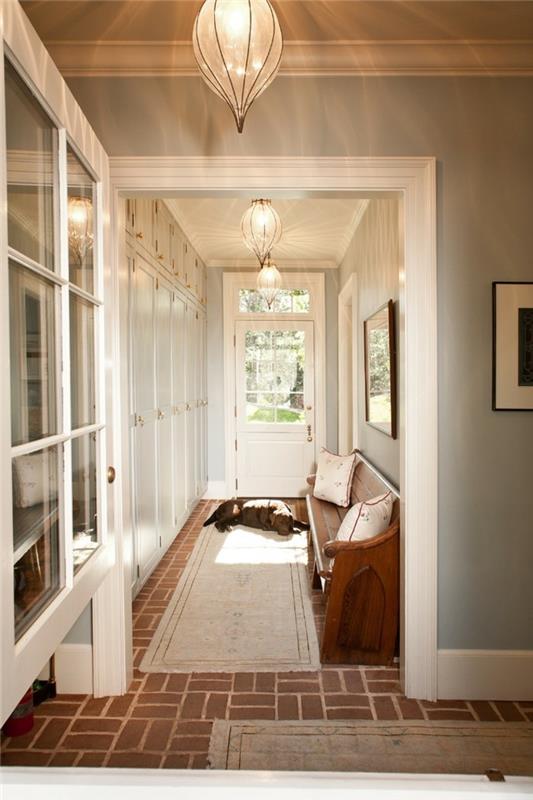 spalni pes, ki leži na bež preprogi, blizu vhodnih vrat, v notranji dvorani s svetlo modrimi stenami in rjavimi keramičnimi tlemi, tekači na dolgih hodnikih, različne omare in lesena sedežna garnitura