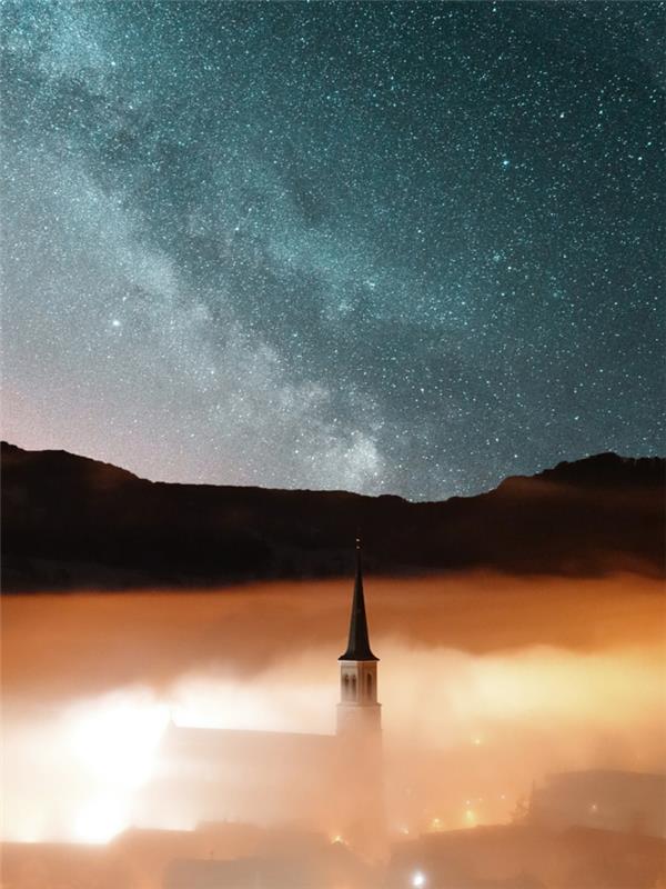 Faro mezzo alla nuvole, cielo sereno con stelle, città con nuvole