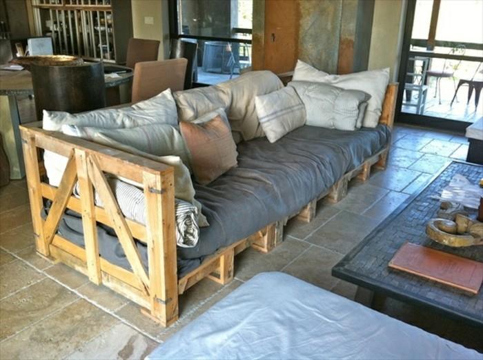 kaimo stiliaus padėklų padėklų sofa, padengta pilka tekstilė, ir daugybė įvairių dydžių pagalvių, netoliese kavos staliukas