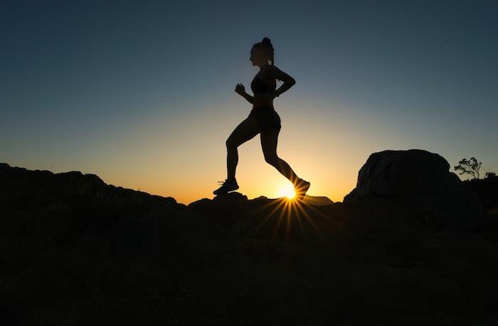 moters siluetas priešais saulę, bėgančią per akmenis