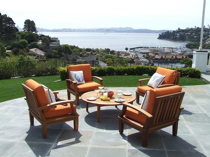 Foto terasa s čudovitim razgledom na morje, okrogla klubska mizica, oranžni blazini za naslanjače, kako urediti svoje oblikovalsko vrtno pohištvo