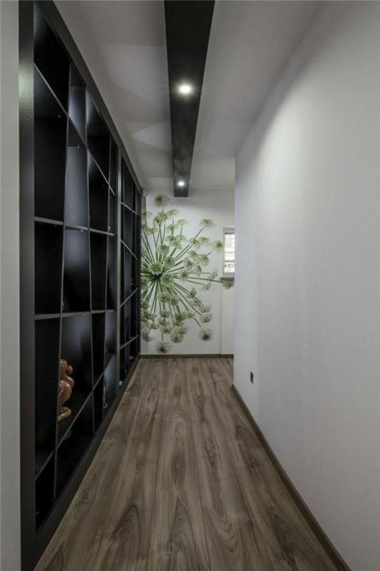 črne asimetrične police, ki pokrivajo steno, na hodniku z lesenimi tlemi, nasprotna stena je navadna bela, tretja stena ima zeleno cvetlično poslikavo, ideje za pohištvo v hodniku