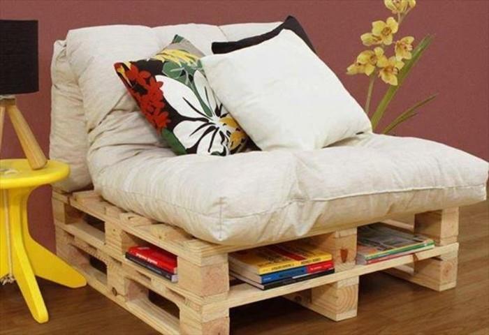 fotelis iš medinių padėklų, su sandėliavimo vieta, baldai iš padėklų, padengti didelėmis, minkštomis šviesiai smėlio spalvos pagalvėmis ir dekoruoti trimis pagalvėlėmis