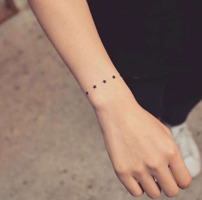 mažos juodos žvaigždės tatuiruotė aplink riešą, maža dilbio tatuiruotė, žmogus dėvi visą juodą spalvą