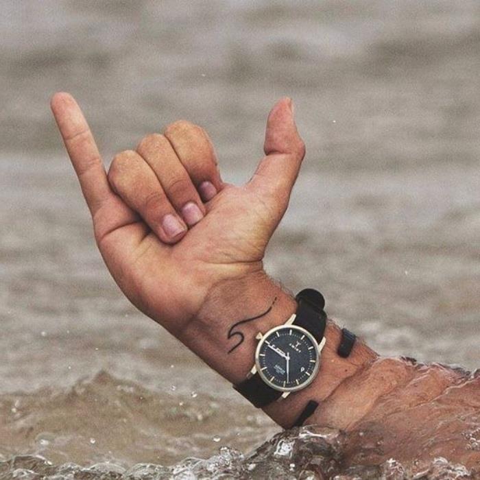 mažos bangos riešo tatuiruotė, maža dilbio tatuiruotė, ranka išeina iš vandens, nešioja juodą laikrodį