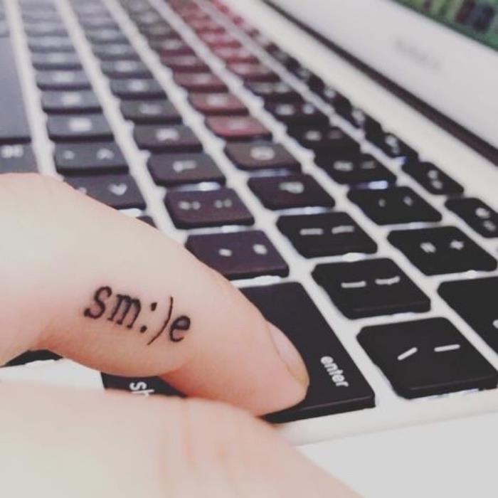 šypsenos piršto tatuiruotė, asmuo spausdina „MacBook“ klaviatūra, maža lotoso gėlės tatuiruotė