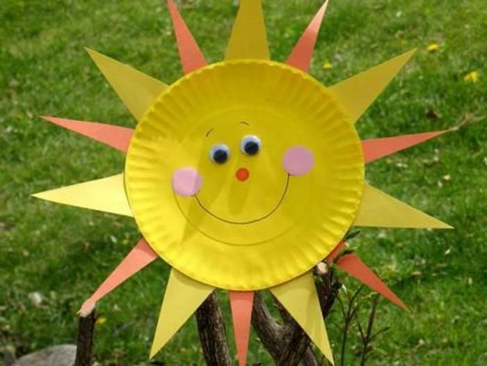 rumena papirnata plošča, okrašena kot nasmejano sonce, z žarki iz rumenega in oranžnega filca, rožnatih lic in nalepljenih oči