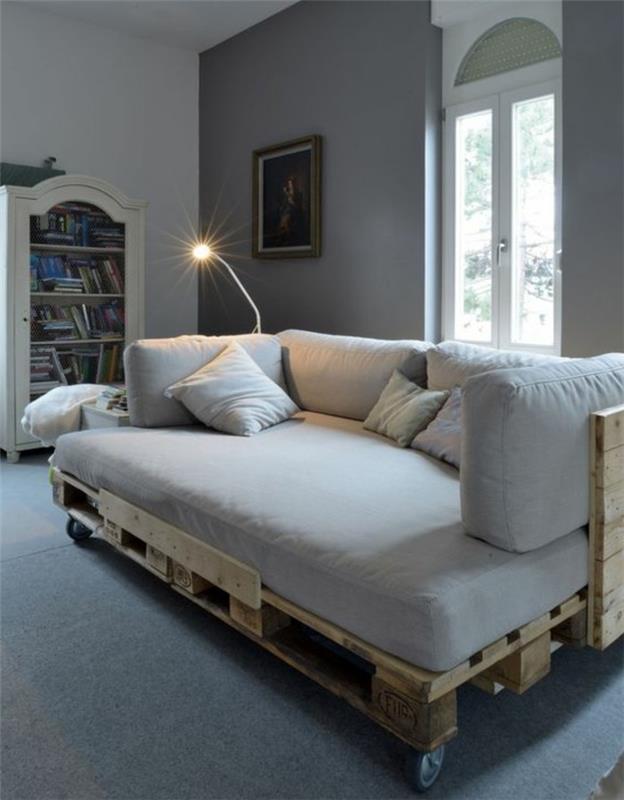 kambarys su skirtingų pilkų atspalvių sienomis, lubomis ir grindimis, kuriame yra pasidaryk pats padėklų sofa, padengta šviesiai pilka tekstilė