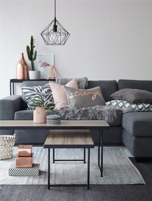 pastelinės rožinės ir kreminės pilkos spalvos pagalvės, ant tamsiai pilkos sofos, šalia dviejų šviesiai smėlio spalvos medinių kavos staliukų, su juodo metalo detalėmis, svetainės dažų spalvos
