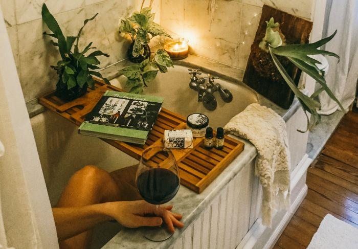 „Cocooning“ vakaro SPA atmosfera jaukus vonios kambarys su SPA grožio produktais žvakės šviesa girlianda knygos žalieji augalai