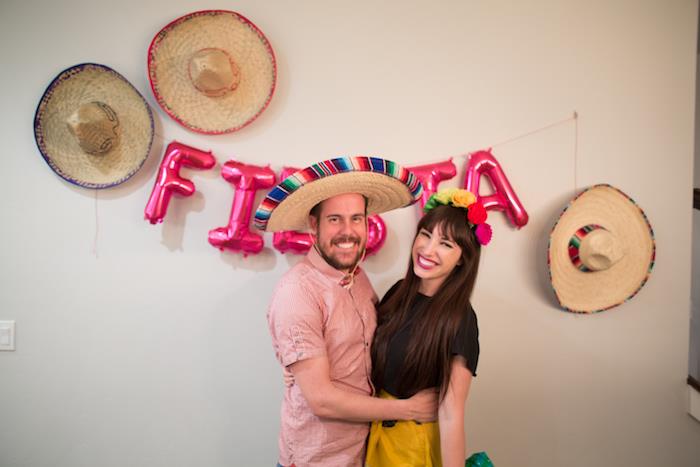 surengti meksikietišką vakarėlį su šiaudinių skrybėlių sienų dekoravimu, fiestos baliono raidėmis, šypsosi moteris ir vyras