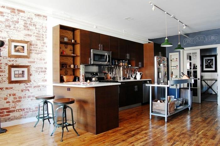 virtuvė su lakuotomis grindimis, pramoninės kėdės, plytų siena, žali pakabinami šviestuvai, L formos sala