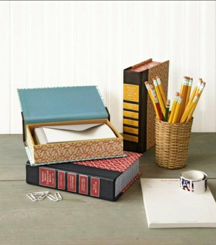 senos knygos virto stacionariomis dėžėmis, ant medinio stalo, šalia pieštuko dėklo, sąvaržėlių ir užrašų knygelės
