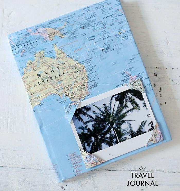žingsnio tėčio dovanų idėjos, rankomis dekoruotas kelionių žurnalas, sudarytas su pasaulio žemėlapiu, ant balto medinio stalo, ant kurio viršelio įklijuota palmės nuotrauka