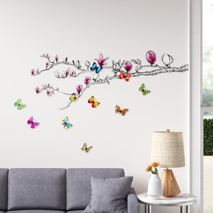 sienos lipdukas, piešiantis mangolijos šaką su drugeliais svetainei su pilka sofa