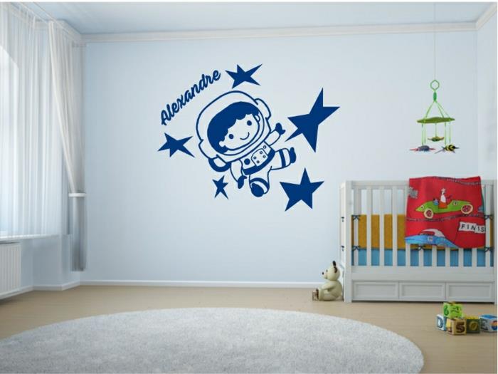Beyaz yatağın üstündeki duvarda kozmosu keşfeden çocuğun ve küçük kozmonotun adının yazılı olduğu bebek odası çıkartmaları
