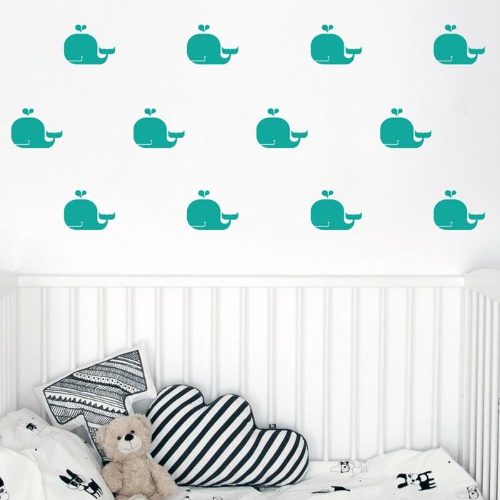 Bir bulut şeklinde ve T harfi şeklinde yumuşak oyuncaklar ve yastıklar ile bir yatağın üzerinde beyaz bir duvar arka plan üzerinde ördek mavisi balina desenleri ile kız yatak odası çıkartmaları