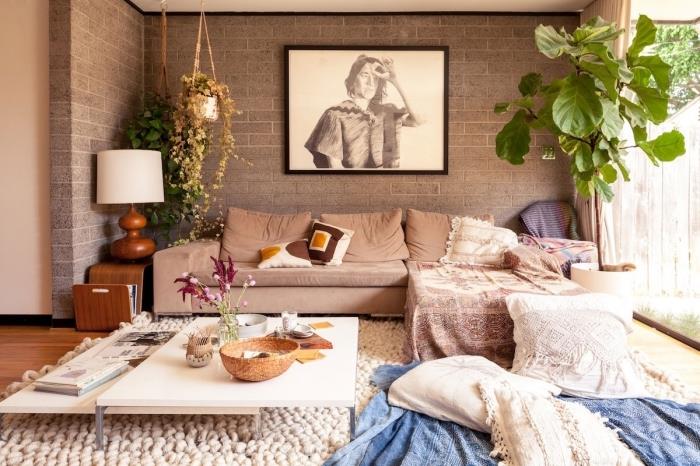 prašmatnus bohemiškas svetainės dekoras pilkomis plytų sienomis su medinėmis grindimis, kampinės sofos modelis, padengtas berberų pagalvėmis