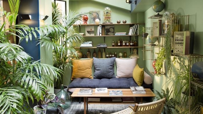etninės dekoracijos idėja mažoje svetainėje su žaliomis sienomis su žaliais augalais, žemos sofos modelis, padengtas pagalvėlėmis