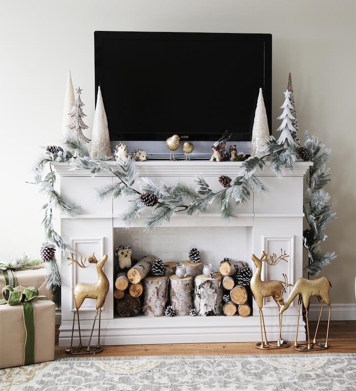 netikras židinys kaip televizoriaus stovas su kalėdiniu papuošimu pušies girlianda ir mediniai rąstai židinyje skandinavišku stiliumi
