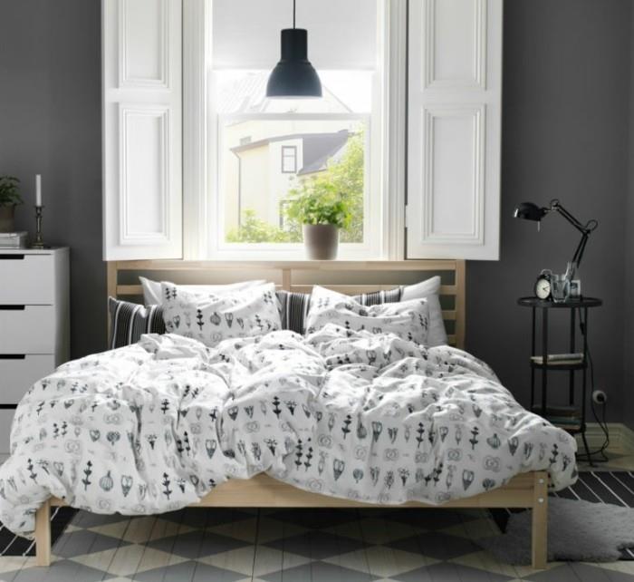 Skandinaviško medžio lovos pakaba prie patalynės aukščio ir kilimas su geometriniais raštais pilkos sienos spalva