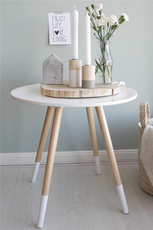 Skandinaviško stalo puošmena, mažas baltas stalas, medinis rąstas, geometrinio rašto žvakidė, vaza su gvazdikų puokšte