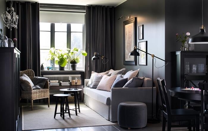 Pastel renklerde minderler ve siyah boyalı ahşap mobilyalarla kaplı açık gri kanepeli koyu duvarlı oturma odası düzeni