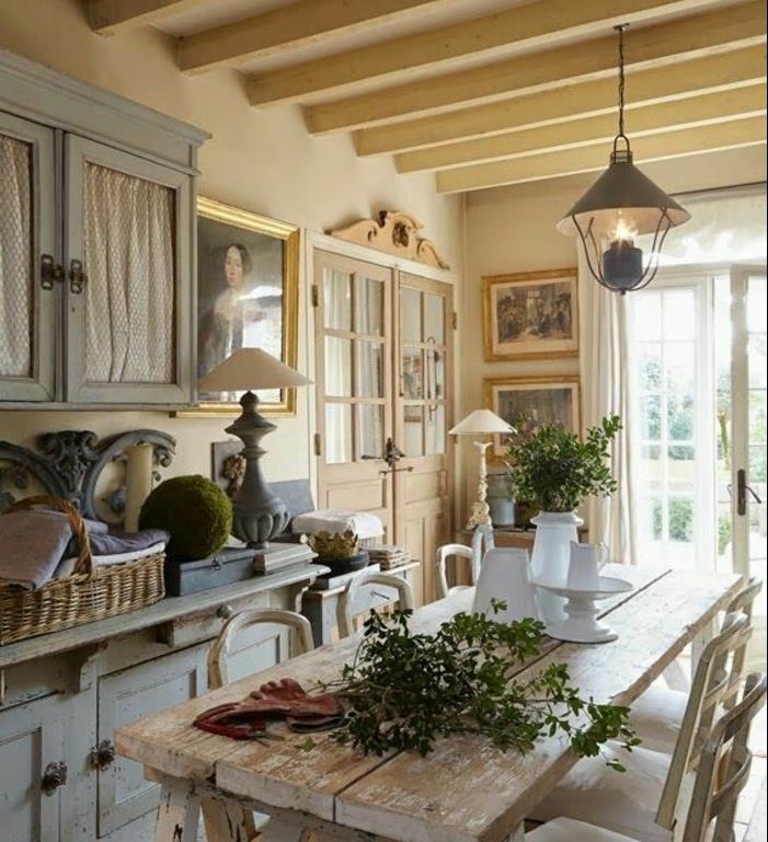 podeželska notranjost, pastelno modra kuhinjska omara, miza in stoli iz surovega lesa, cvetlični okras, izpostavljeni tramovi, viseča luč