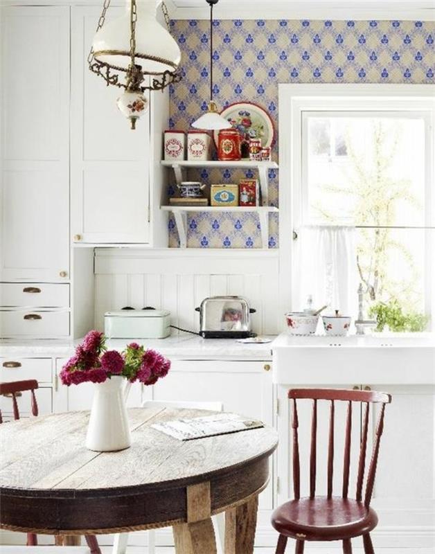 ideja okrogle elegantne podeželske mize, rdeči stoli, bež ozadje z modrimi vzorci, bela kuhinjska sprednja stran, šopek rož