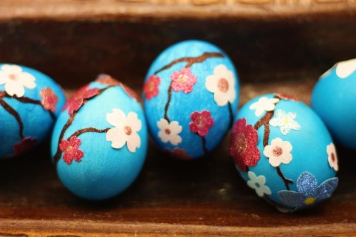 pavyzdys virtas kiaušinis su šviesiai mėlynos spalvos dažais su gėlėmis ir popieriaus šakomis bei spalvotu audiniu