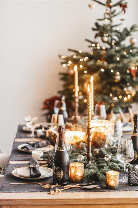 medinis valgomasis stalas, papuoštas Kalėdoms, uždegtos žvakės, didelė eglutė, dirbtinės pušies šakos