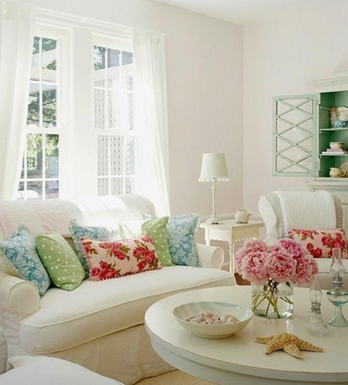 beli leseni kavč in miza, večbarvne blazine, šopek potonik, pastelno zelena komoda, bele zavese