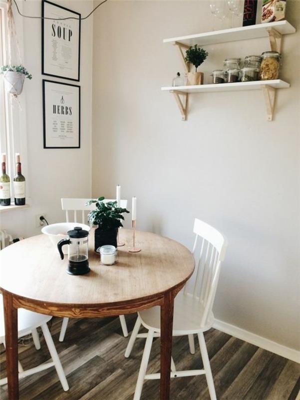 apvalus stalas-iš medžio masyvo-baltos-kėdės-smėlio-siena-žalia-augalai-kambarinės žvakės-dekoratyvinės